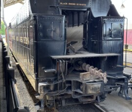 Lit by the early afternoon sun, N&W Class A #1218's tender is seen here with the stoker's augur visible. The locomotive and tender are presently disconnected under the train shed named for W. Graham & Bob Claytor. (5/31/26, Phil Bell Photo)